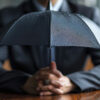 A businessman in professional attire holding an umbrella, symbolizing protection and understanding of garage insurance quotes.